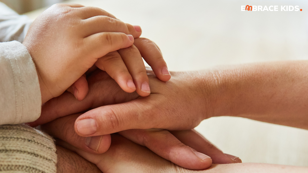 Three sets of hands stacked on top of each other, with adult and child hands layered together, representing three generations.